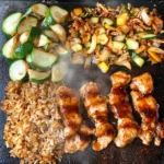 Hibachi chicken with fried rice and sautéed vegetables cooking on a Blackstone griddle